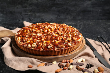 Wooden board of sweet tart with different nuts and caramel on black background