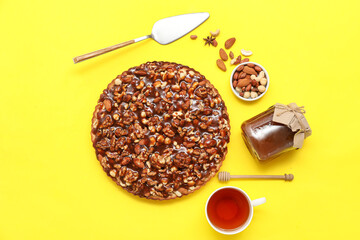 Sweet tart with different nuts and cup of tea on yellow background