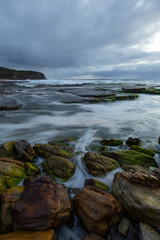 Wave water flowing around the rocks on the shore.