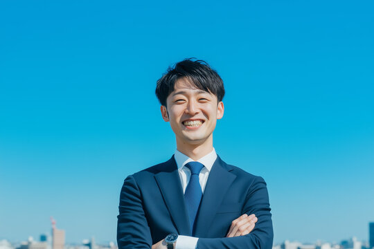 笑顔で腕組みをする若いビジネスマン、アジア人、日本人、空、都市