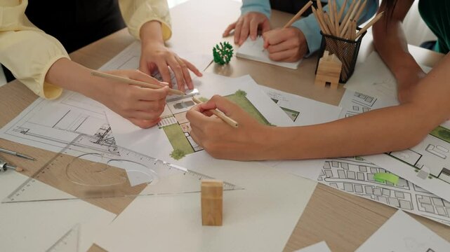 Smart architect and safety engineer discussion about building blueprint on table with architectural document, measurement tools and wooden block scatter around at modern office. Closeup. Delineation.