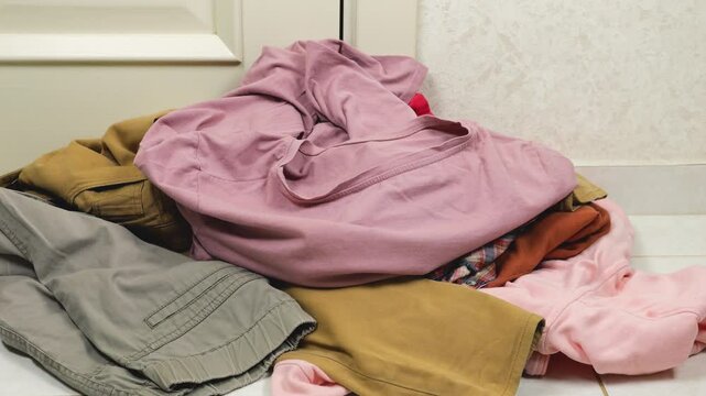 Colored shirts and t-shirts are thrown on a pile of laundry on the floor. The theme of washing, sorting clothes and cleaning the house.