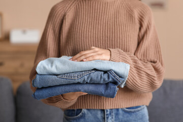 Fototapeta premium Young woman with stack of jeans at home, closeup