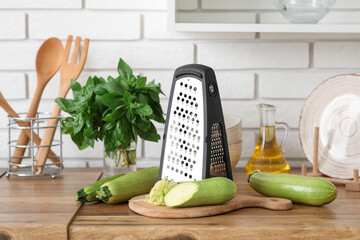 Grater with zucchini on table near white brick wall in kitchen