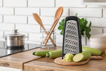 Grater with zucchini on table near white brick wall in kitchen