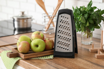 Grater, cutting board and fresh apples on wooden table in kitchen