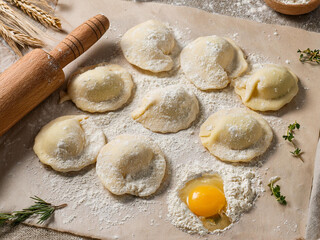 Homemade ravioli pasta on a floured countertop with a wooden rolling pin and fresh egg yolk, ready for cooking.
