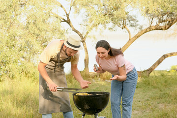 Young couple cooking food on grill at barbeque party