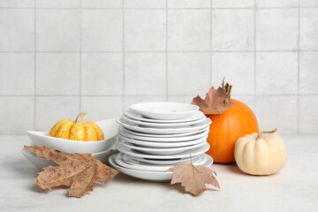 Stack of dishes with autumn decor and pumpkins on table against white tile background