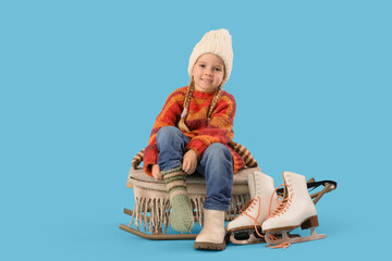 Cute little girl in winter clothes putting warm sock on blue background