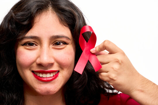 Young Latin woman smiling, holding red World AIDS Day ribbon - Powered by Adobe