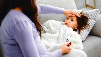 Sad little girl laying on sofa, feeling ill, complaining her pregnant mom, expecting mother...