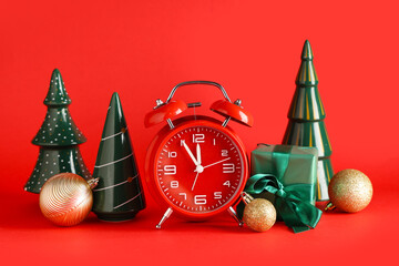 Alarm clock, gift box, balls and ceramic Christmas trees on red background