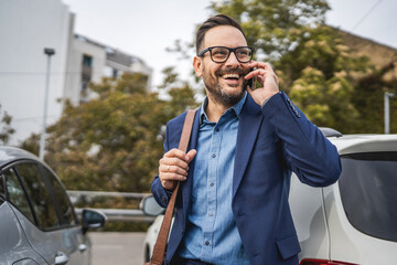 Adult businessman stand in the parking lot and talk on mobile phone