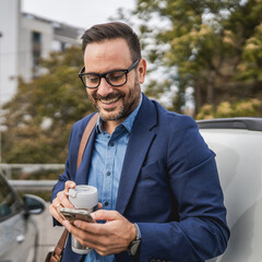 Adult businessman stand in the parking lot and use mobile phone