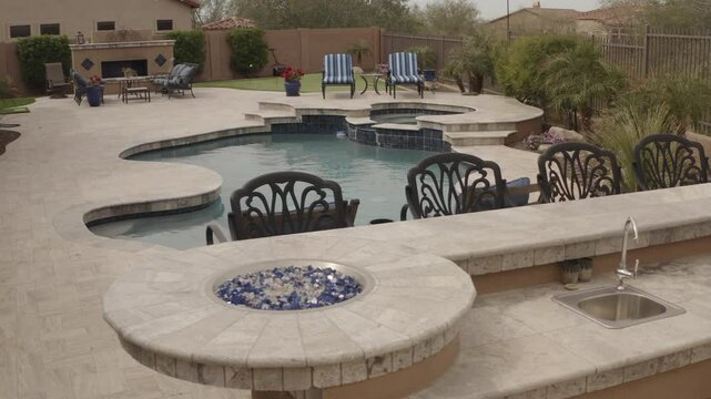 An arial view of a desert landscaped yard in Arizona featuring a travertine tiled pool deck, spa, outdoor kitchen and fireplace.