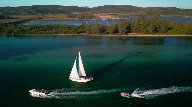 Two boats sailing along the coastline of Itajuru Canal in Cabo Frio, Brazil, with a backdrop of lush greenery.