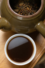 bowl of Chinese herbal tea and an enamel pot with herbs nearby at vertical composition