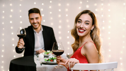 Attractive young woman and handsome man having romantic dinner together, posing to camera in restaurant, selective focus on girl