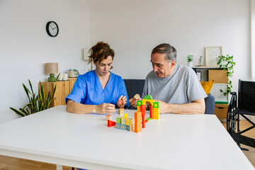 Female caregiver and senior man playing wooden shape puzzles game for dementia prevention