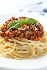 Tasty pasta bolognese with basil on white plate, closeup