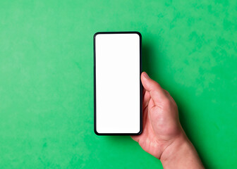 Hand holding a phone with blank screen on a green background