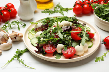 Tasty salad with arugula, lettuce, mozzarella cheese and vegetables on white table, closeup