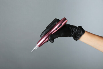 Professional cosmetologist holding permanent makeup machine on grey background, closeup