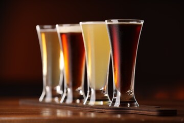 Glasses with different types of beer on wooden table against color background, closeup