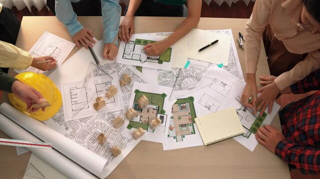 Architect and safety engineer discussion about building construction use blueprint on table with architectural document, measurement tool and wooden block scatter around at modern office. Delineation.