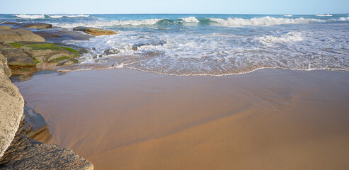 Surf waves breaking at sea and over rocks and rolling onto sandy beach east coast of Australia