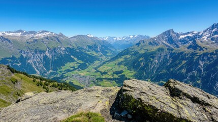 Naklejka premium A panoramic view of a valley nestled between snow-capped mountains, seen from a rocky cliff.