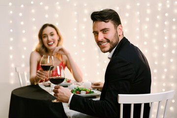 Beautiful young couple with glasses of red wine on romantic date in restaurant, celebrating anniversary or valentine's day together, selective focus