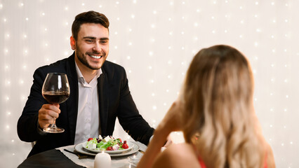 Handsome Man Making Toast For Love On Romantic Dinner With His Girlfriend in Restaurant, Celebrating Valentine's Day Together, Selective Focus