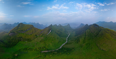 A breathtaking aerial view of a lush green valley surrounded by towering mountains. A winding river cuts through the serene landscape under a clear, expansive sky, creating a sense of natural beauty