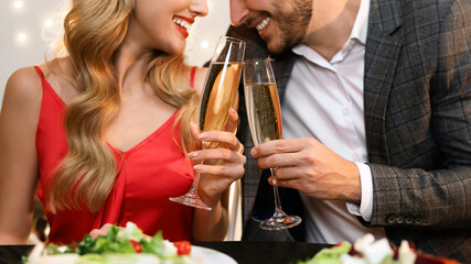 Champagne glasses in hands of unrecognizable couple at romantic dinner. Valentine's Day celebration, loving pair dining in restaurant