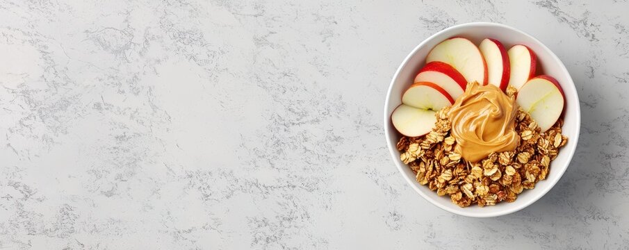 A bowl of sliced apples topped with peanut butter and granola on a textured surface, showcasing a healthy and appealing snack option.
