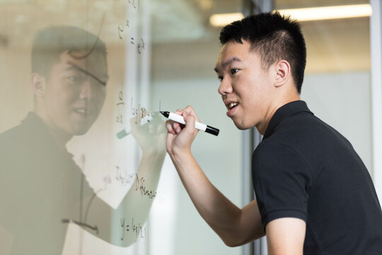 A young student doing a math question on a glass whiteboard