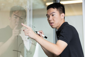 A young student doing a math question on a glass whiteboard