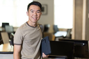 A smiling high school student holds a laptop in his hands in the classroom