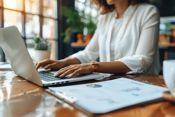 Fototapeta premium Woman Typing on Laptop with Documents in Cafe, Remote Work, Businesswoman in Casual Attire, Professional Workspace, Productivity