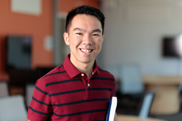 Fototapeta premium Portrait of a smiling college student in a classroom holding a book