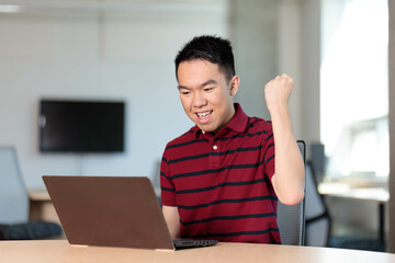 A college student sits at a table and makes a fist pump excitedly