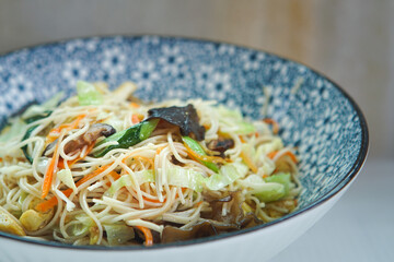 Asian vegetarian food, fried noodles with vegetables, tofu, mushrooms, sesame and pepper close-up on plate.