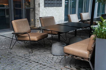 Outdoor café setting with empty tables and chairs, surrounded by  plants.