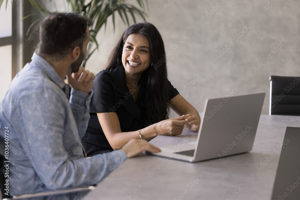 Wall mural happy young middle eastern business woman speaking to male colleague at laptop, discussing collabora