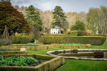 Fototapeta premium Picturesque garden with neatly trimmed hedges, a small pond, and a white house in Dunrobin castle