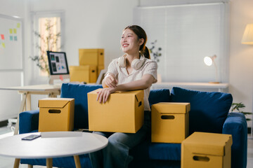 Young woman taking a break on her sofa in a new apartment surrounded by unpacked boxes, happily envisioning her future in her new home