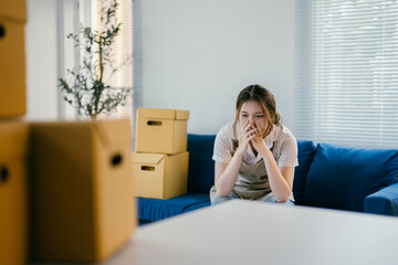 Young woman is sitting on her couch, surrounded by moving boxes, feeling overwhelmed by the stress of moving to a new home