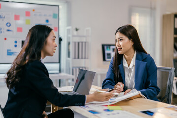 Two young businesswomen are having a serious conversation in a meeting, analyzing charts and data on a desk with a laptop
